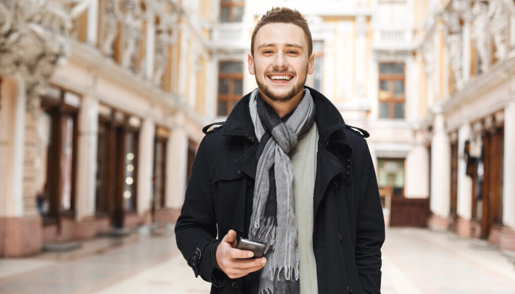Front view of cheerful man holding phone and looking straight.