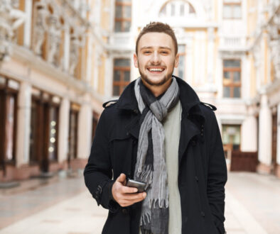 Front view of cheerful man holding phone and looking straight.