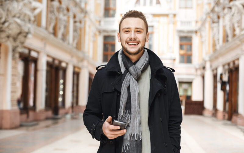 Front view of cheerful man holding phone and looking straight.